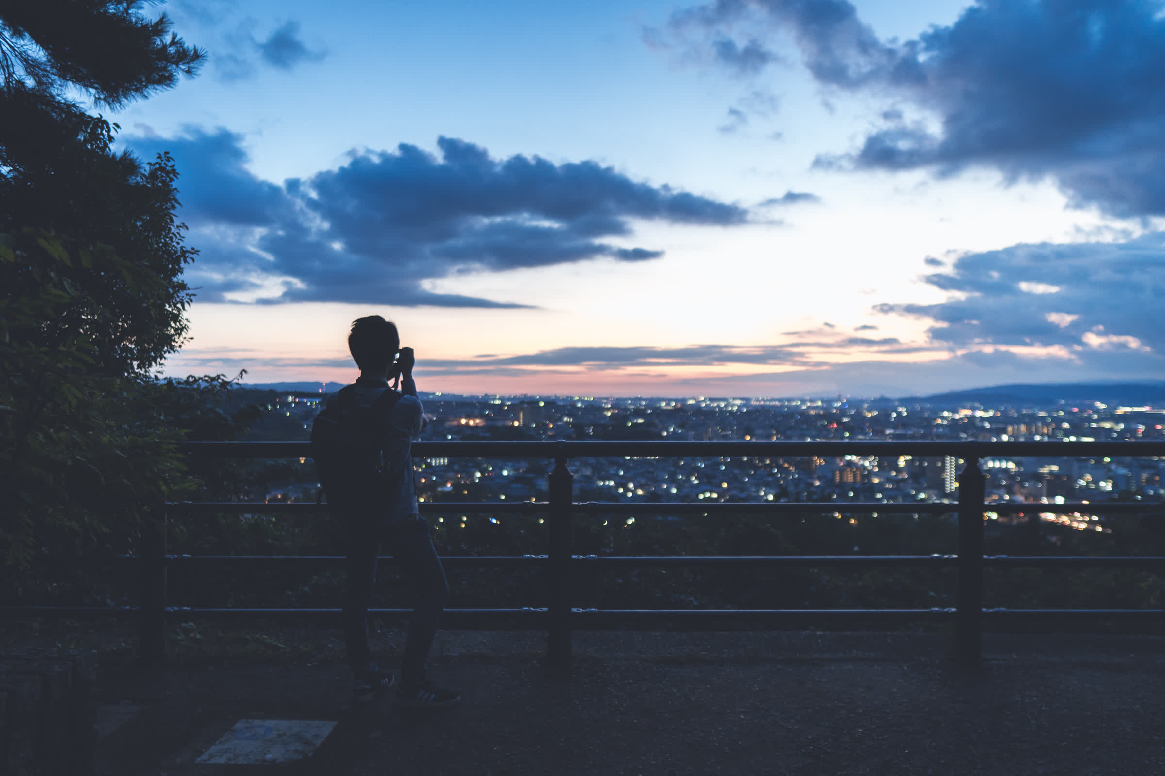 日没、暗くなる街の灯りを背景に立っている人を後ろからとらえた写真