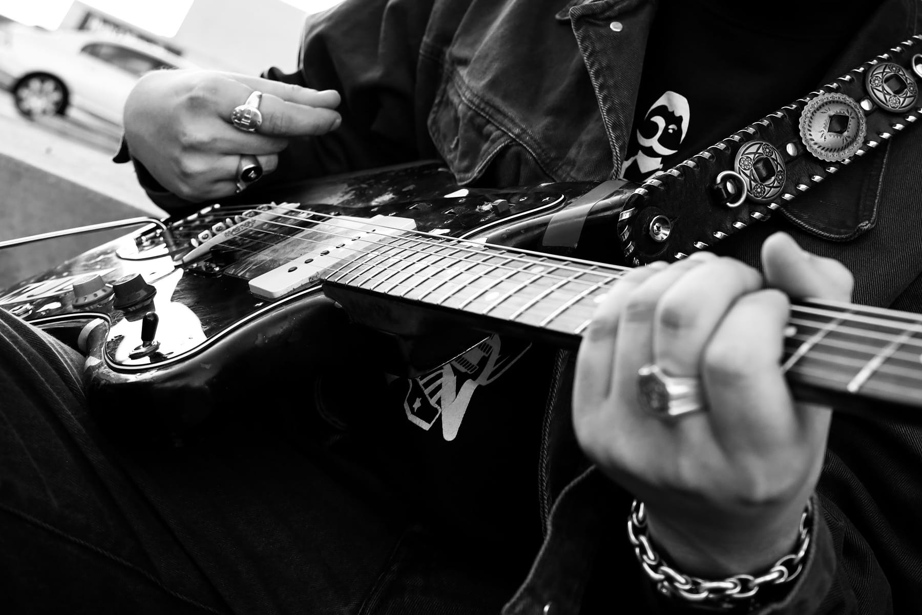リングやブレスレットをつけた手でFender Jazzmasterをかき鳴らす人の白黒写真