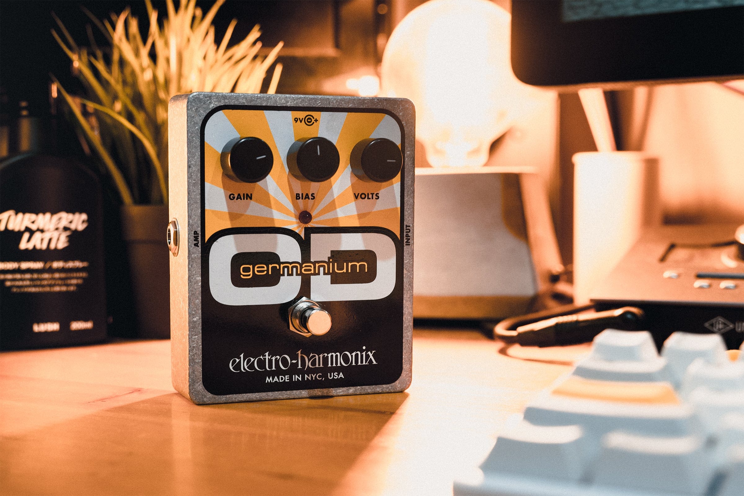 テーブルランプを背景にキーボードやオーディオインターフェースが置かれた中で自立しているElectro Harmonix Germanium ODの写真